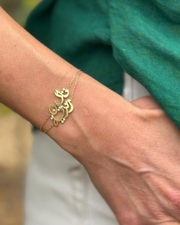 Two layered gold bracelets with Arabic names, worn on the wrist