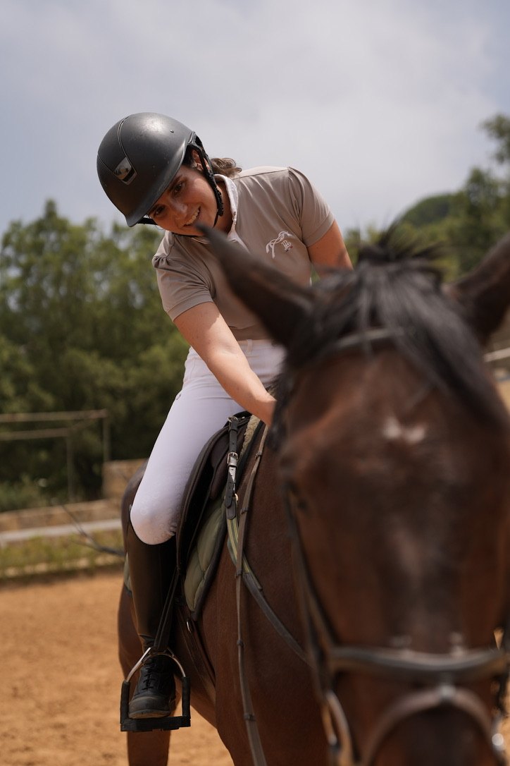 A smiling rider leaning forward to pat her horse in the arena