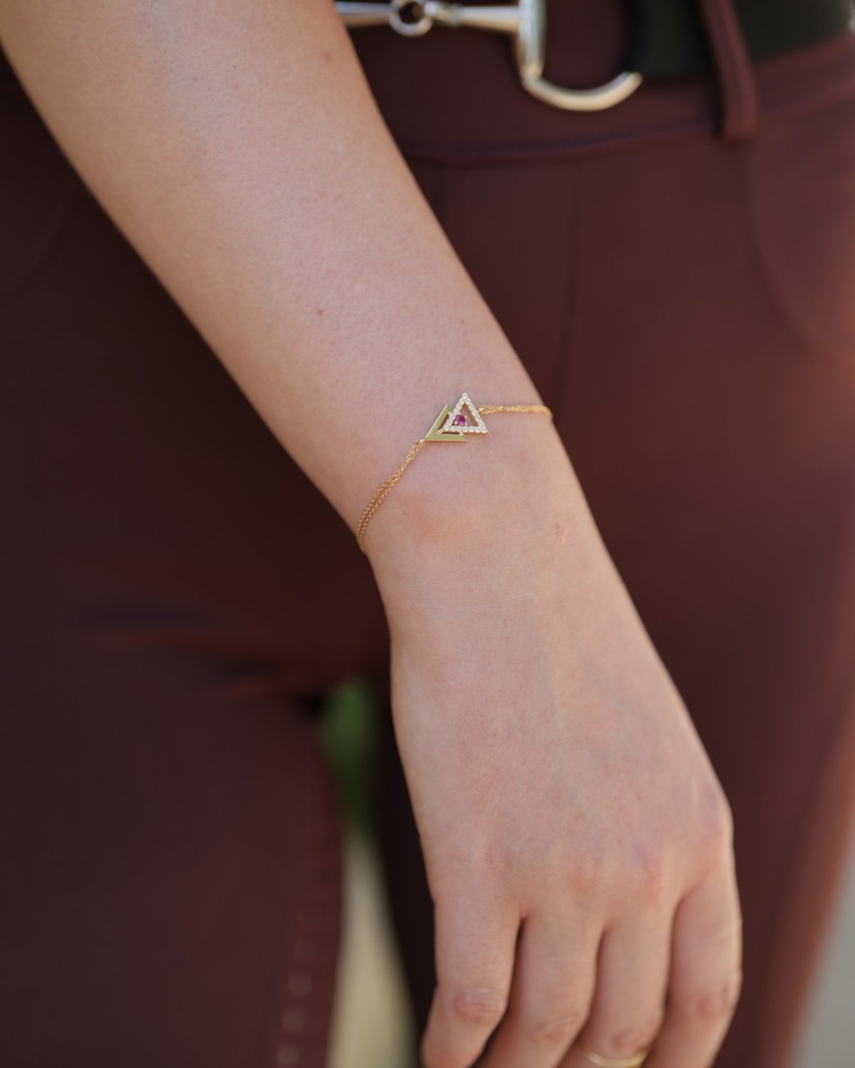 Gold arrow bracelet with a red stone, in warm light