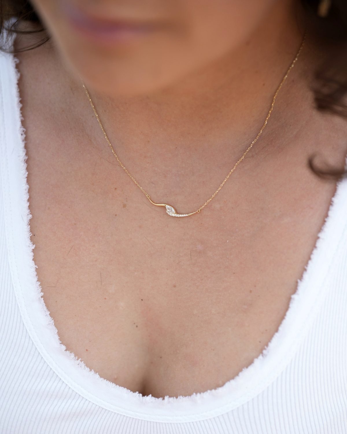 Gold curved marquise necklace set with zircon, worn with a white top