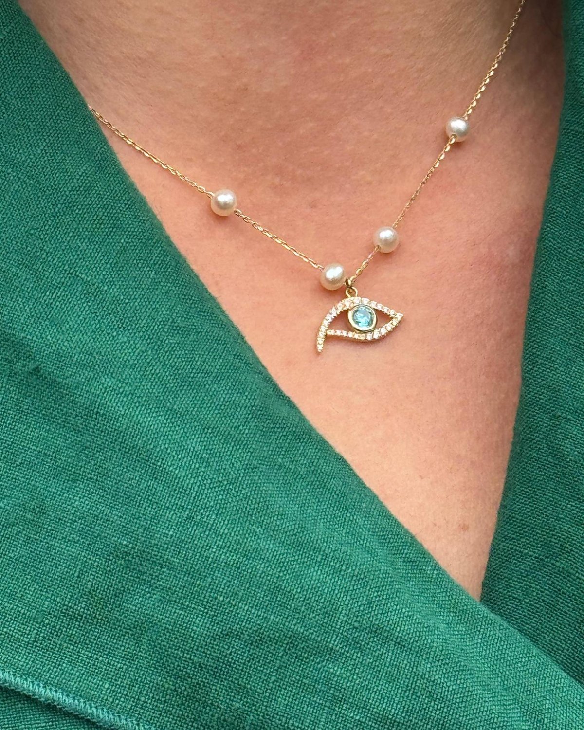 Gold eye necklace with pearls and a turquoise centre, in warm light