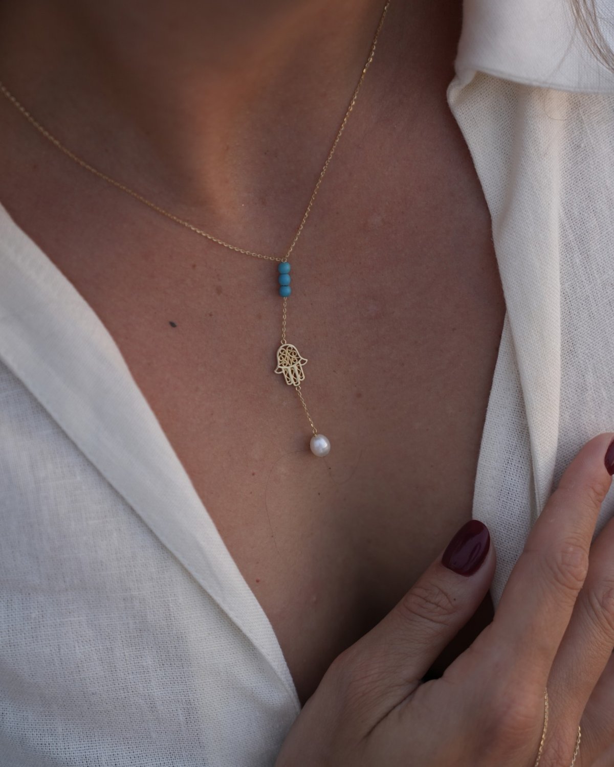 Y-shaped gold Fatima hand necklace with blue freshwater pearls, worn with a white shirt