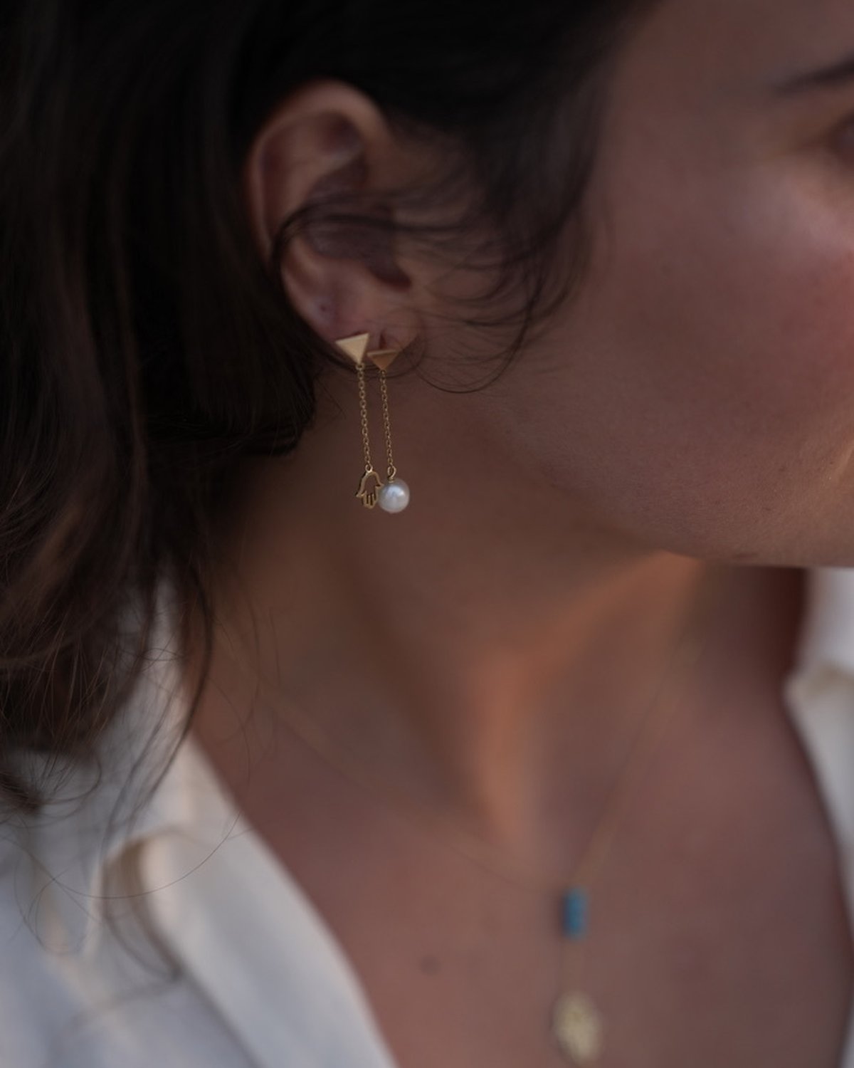 Asymmetric gold Fatima and pearl drop earrings, worn