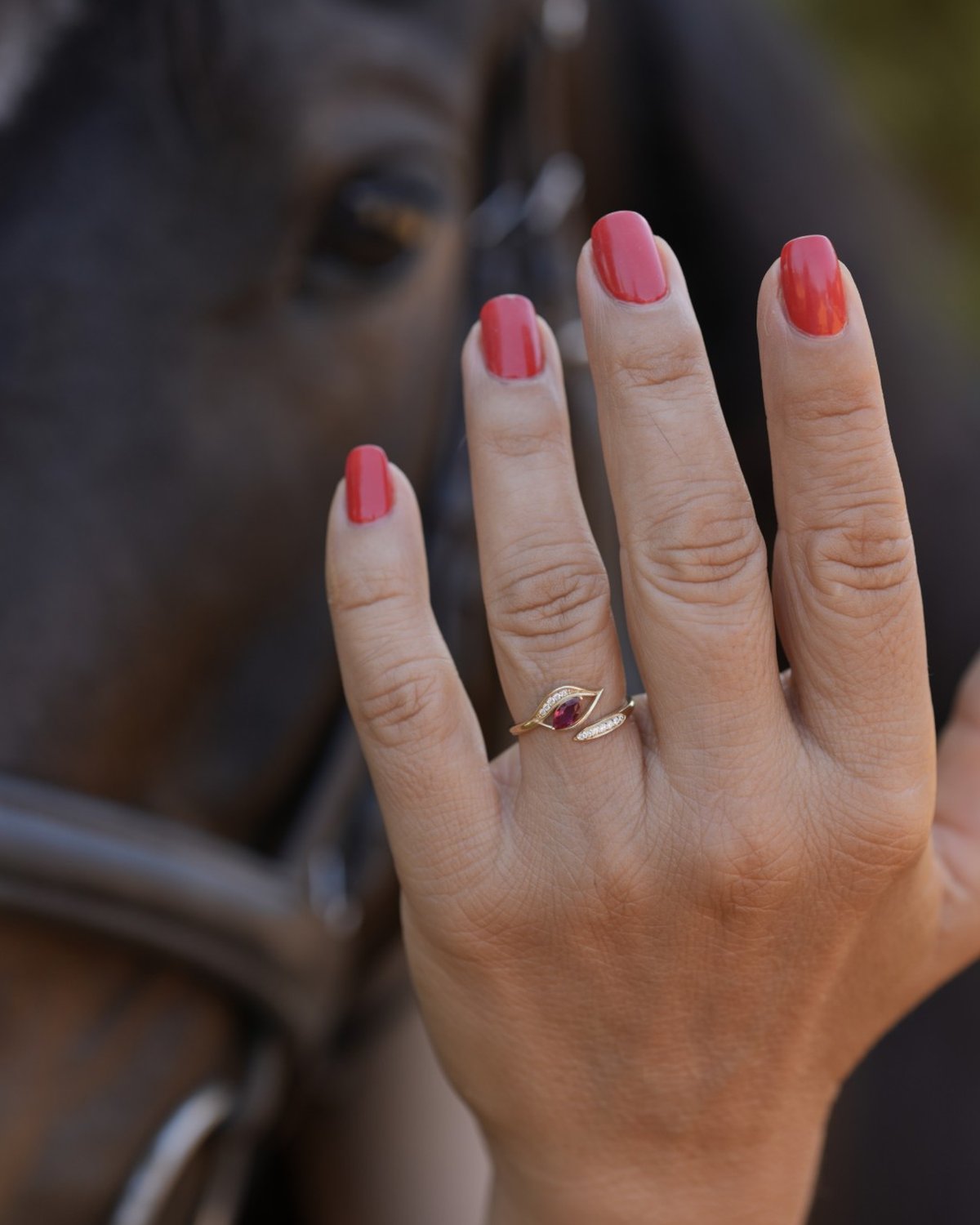 Gold horse eye ring with a red stone, worn on a hand resting on a horse