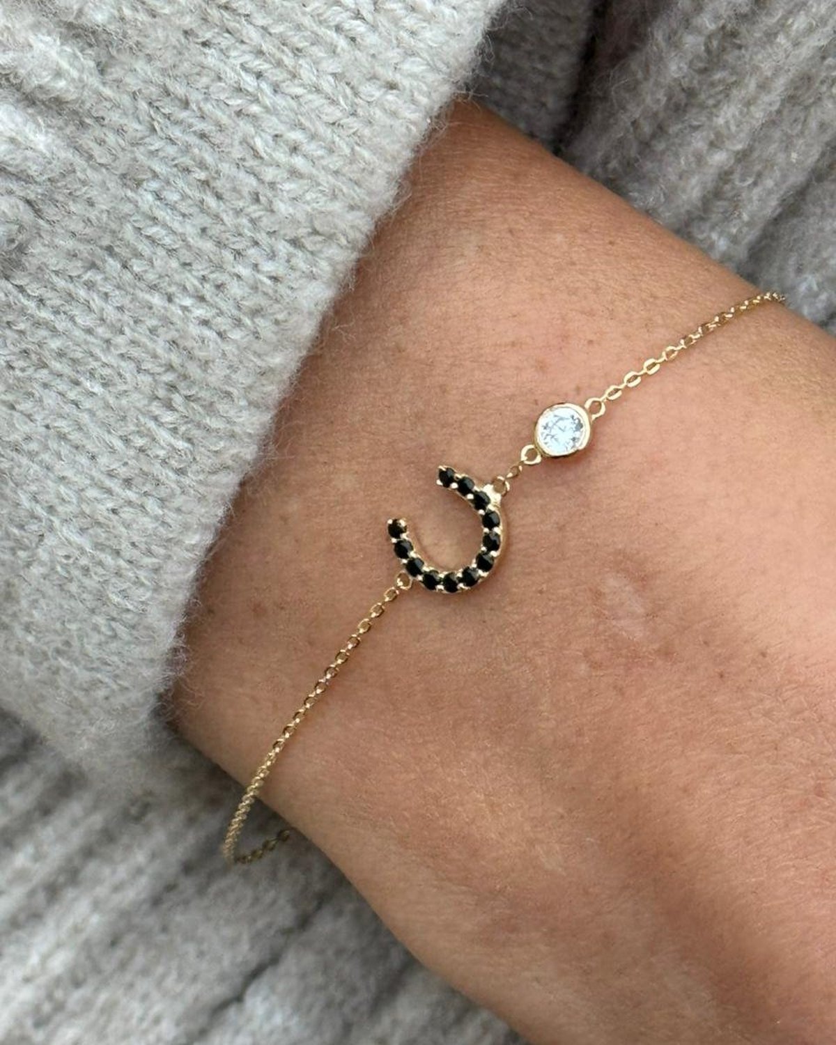 Gold chain bracelet with a black stone horseshoe and a white stone, on the wrist