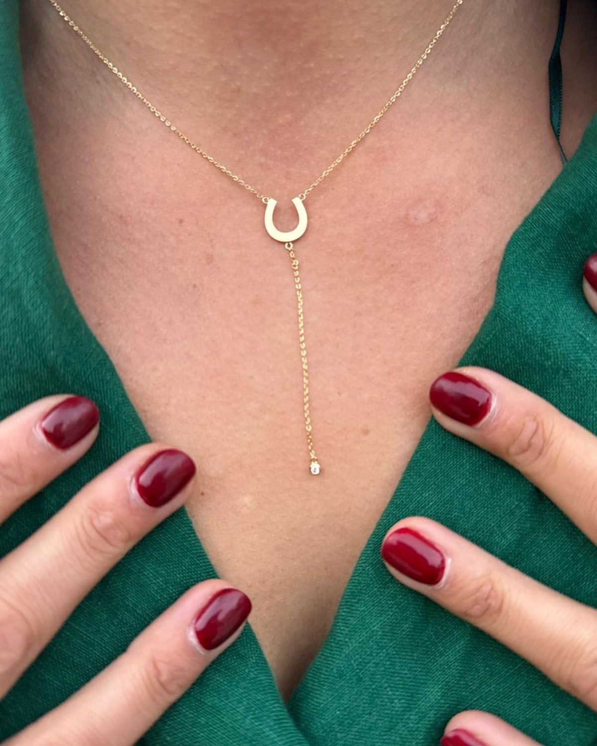 Gold horseshoe pendant necklace with a long drop, worn with a green top