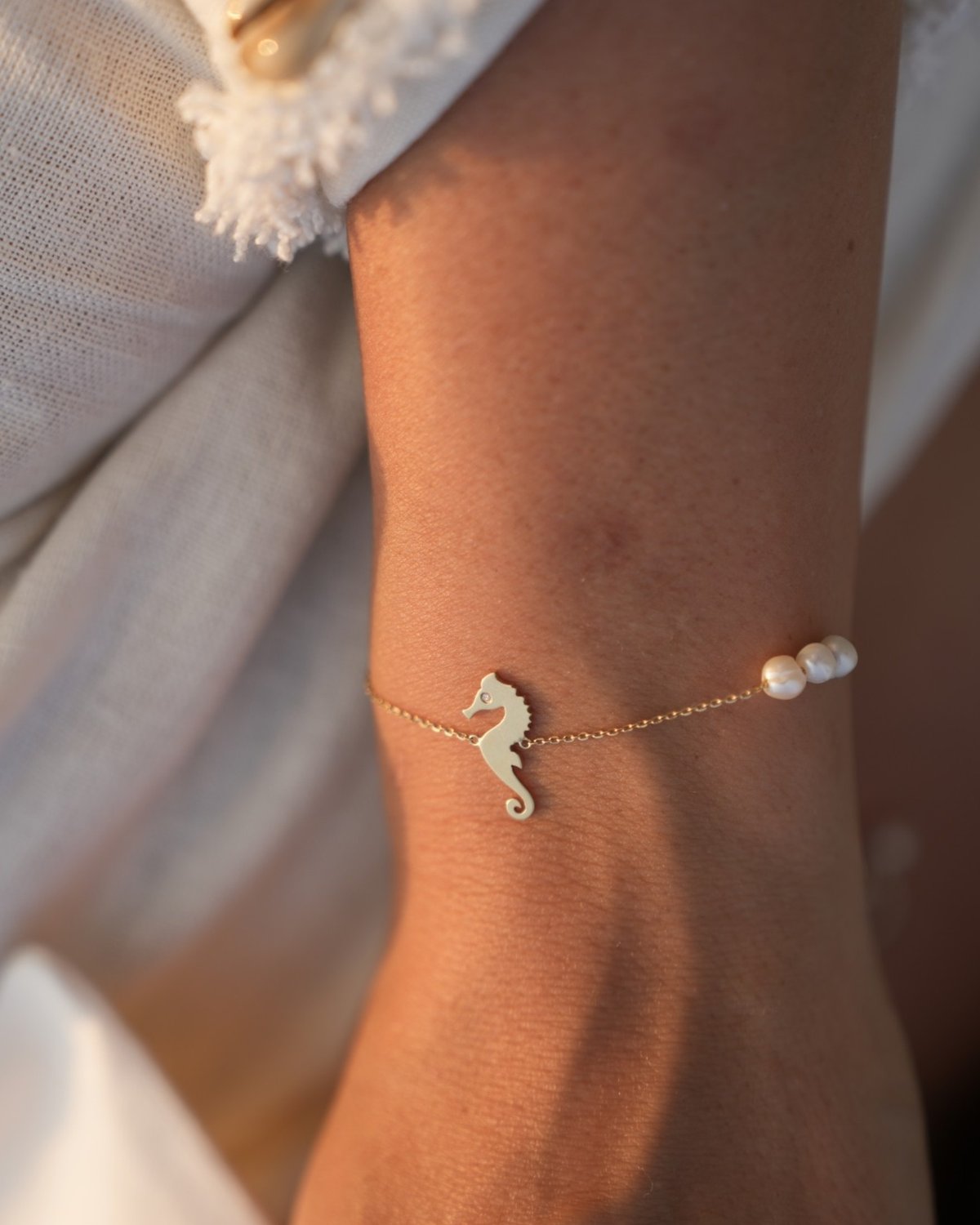 Gold seahorse bracelet with white pearls, on the wrist