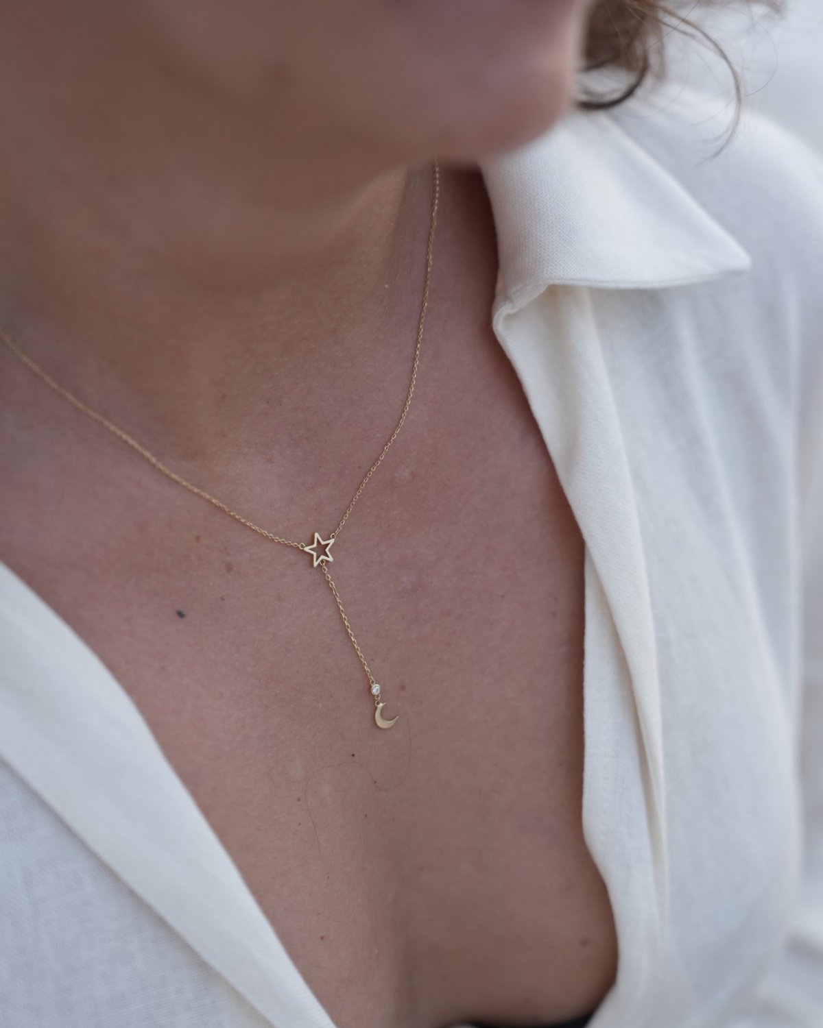 Y-shaped gold star and moon necklace displayed on a candle