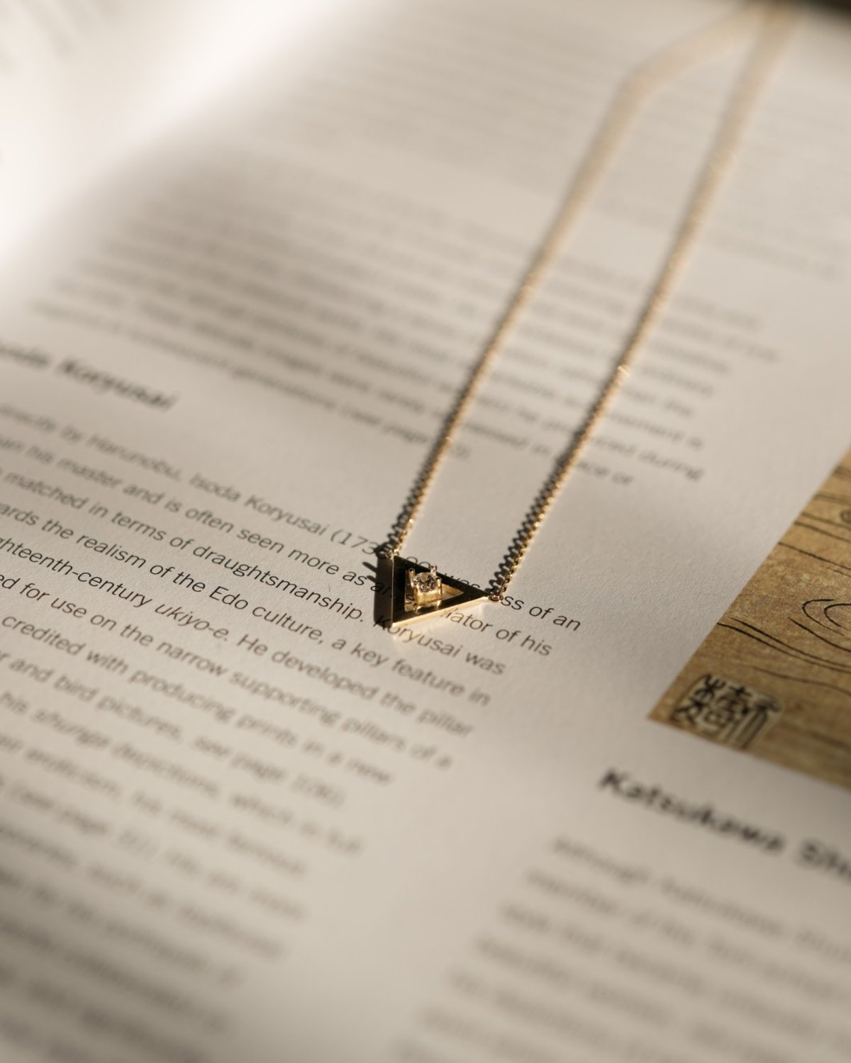 Gold open triangle necklace with a white stone, on an open book